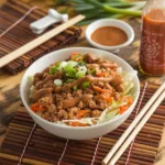 Egg Roll in a Bowl with Creamy Chili Sauce served in a white bowl on a bamboo mat, surrounded by Asian-inspired ingredients and utensils