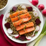 Zesty Smoked Salmon and Lentil Salad with radishes, beets, and dill vinaigrette in a white bowl on wooden table.
