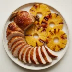 Honey-glazed guinea fowl supreme sliced and served with grilled pineapple rings on a white plate.